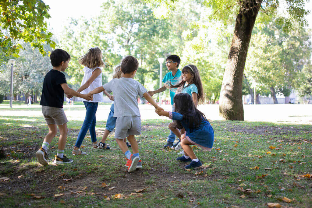 Jak děti motivovat k pohybovým aktivitám happy children playing together outdoors dancing around grass enjoying outdoor activities having fun park kids party friendship concept