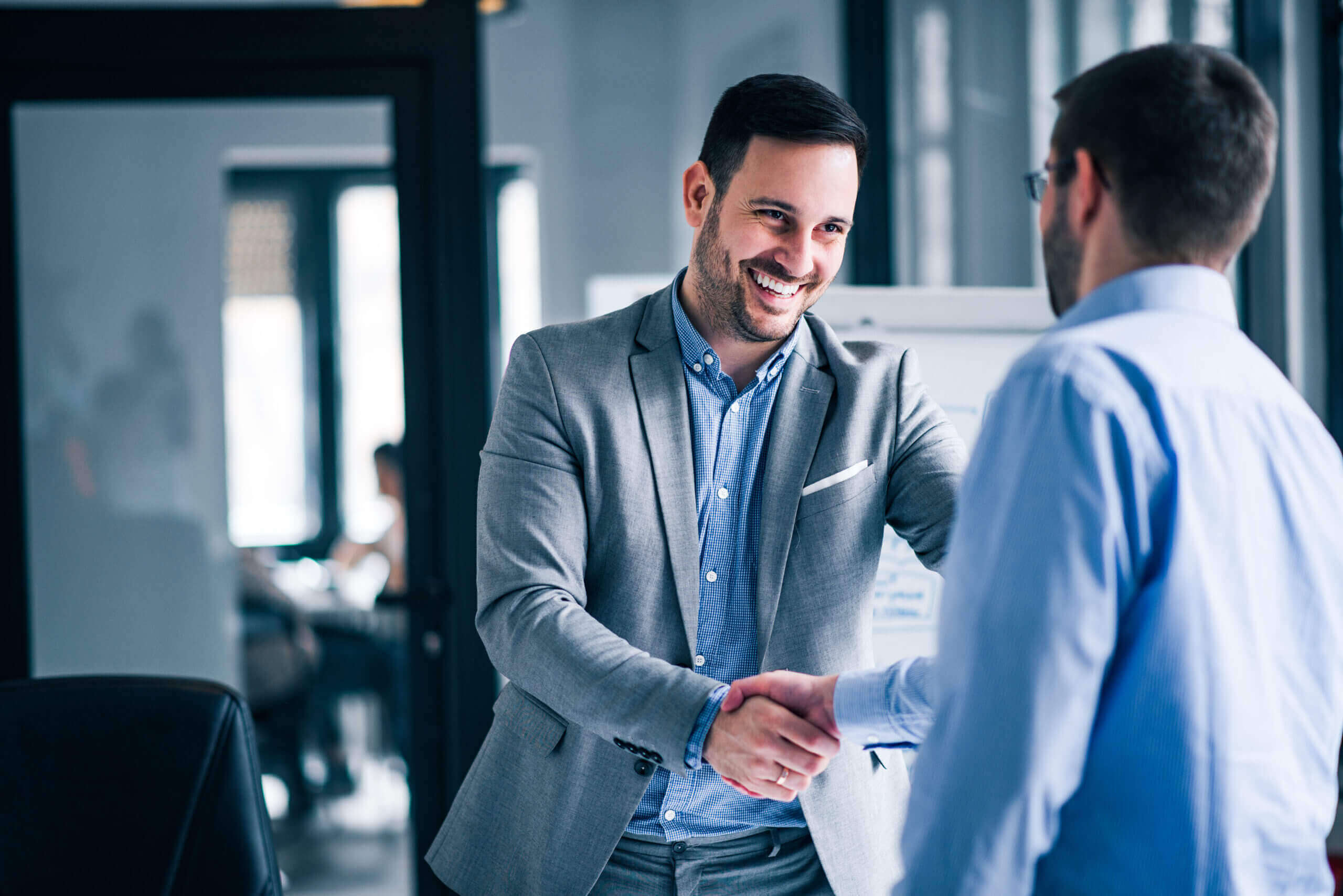 two smiling businessmen shaking hands while standing office scaled