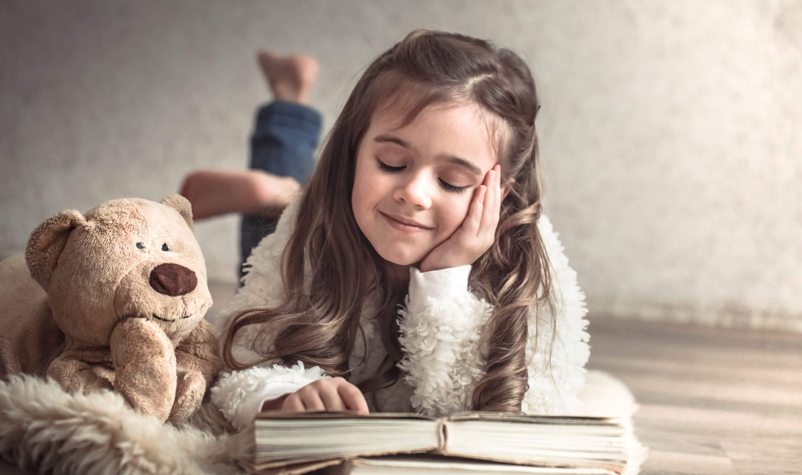 little girl reading book with teddy bear floor concept relaxation friendship scaled
